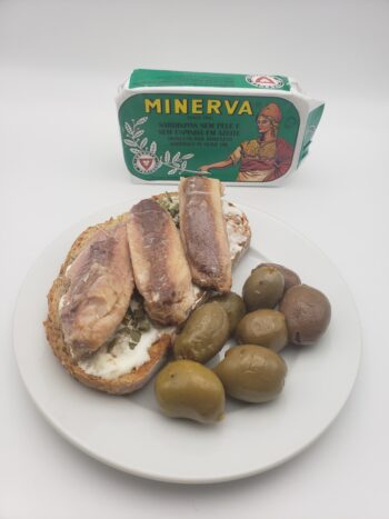 Image of Minerva skinless boneless sardines in olive oil plated on toast with sour cream, chives, and olives