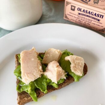 Image of a serving suggestion for Olasagasti Bonito del Norte showing chunks atop smashed avocado on thin dark rye toast.