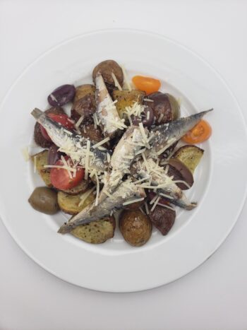 Image of Espinaler small sardines 14/16 plated with roasted potatoes, olive, tomatoes, and parmesan