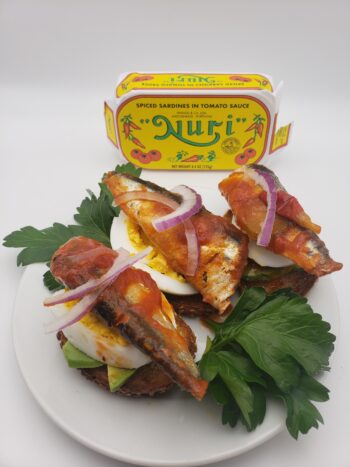 Image of Nuri sardines in spiced tomato sauce on crostini with hardboiled egg, avocado, and red onion