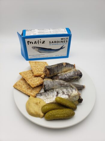 Image of Matiz sardines with spanish olive oil on a plate with crackers, pickles, and mustard
