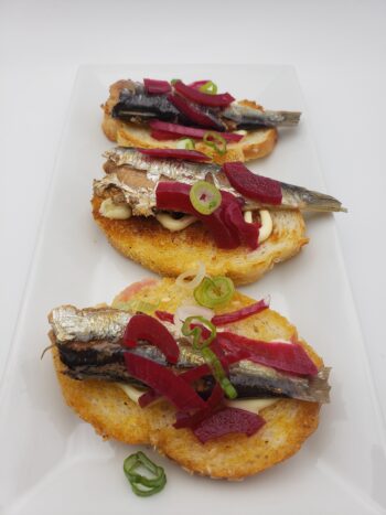 Image of Mouettes d'arvor sardines in peanut oil on crostini with pickled red onion and chive cream cheese