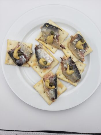 Image of bon appetit sardines in sunflower oil on saltines wiht mustard and capers