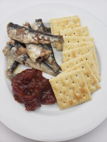 Image of Les Mouettes d'arvour vintage sardines saison 2021 plated with tomato jam and crackers